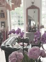 Una habitación con un sofá de cuero verde, orquídeas púrpuras y un espejo grande.