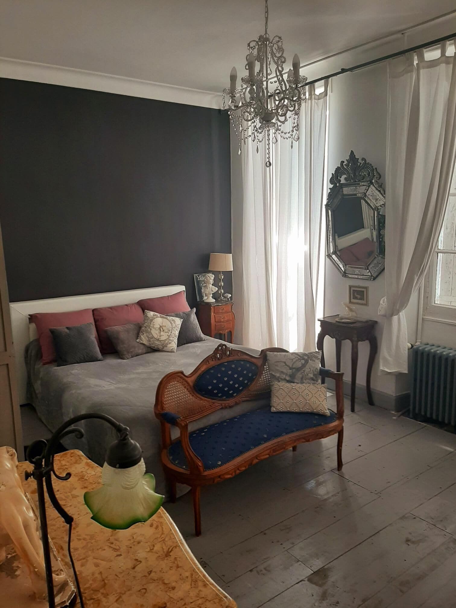 Camera da letto con un letto grande, un divano in legno, un lampadario, uno specchio e un termosifone.