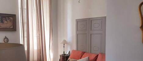 Un dormitorio con cama, mesita de noche, cómoda, candelabro y ventana con cortinas.