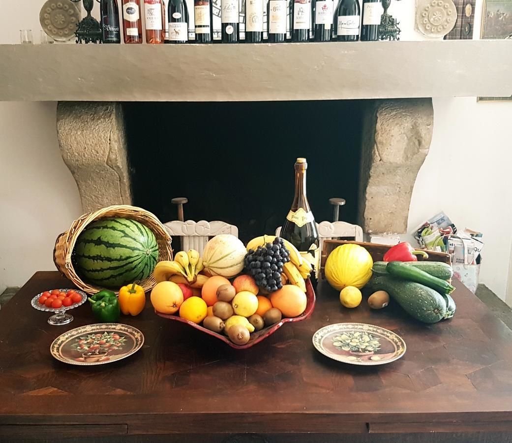 A table with a variety of fruits and vegetables, a bottle of wine, and a fireplace mantel with wine bottles.