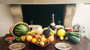 A table with a variety of fruits and vegetables, a bottle of wine, and a fireplace mantel with wine bottles.