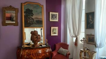 A room with a purple wall, a wooden dresser, a red armchair, a white chair, and a chandelier.