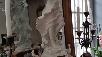 A marble statue on a pedestal with a clock, surrounded by other statues and candelabras in a room with large windows.