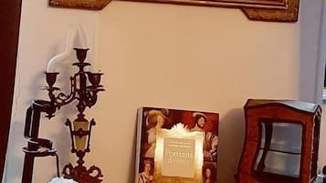 Ein Zimmer mit einem großen, verzierten Spiegel, einem Buch mit dem Titel 'Portraits de Coeur', einem dekorativen Kerzenleuchter und einer kleinen, weißen Figur auf einer Marmorplatte.
