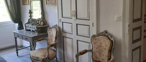 A room with two ornate chairs, a table with a teapot, and a door with a mirror.