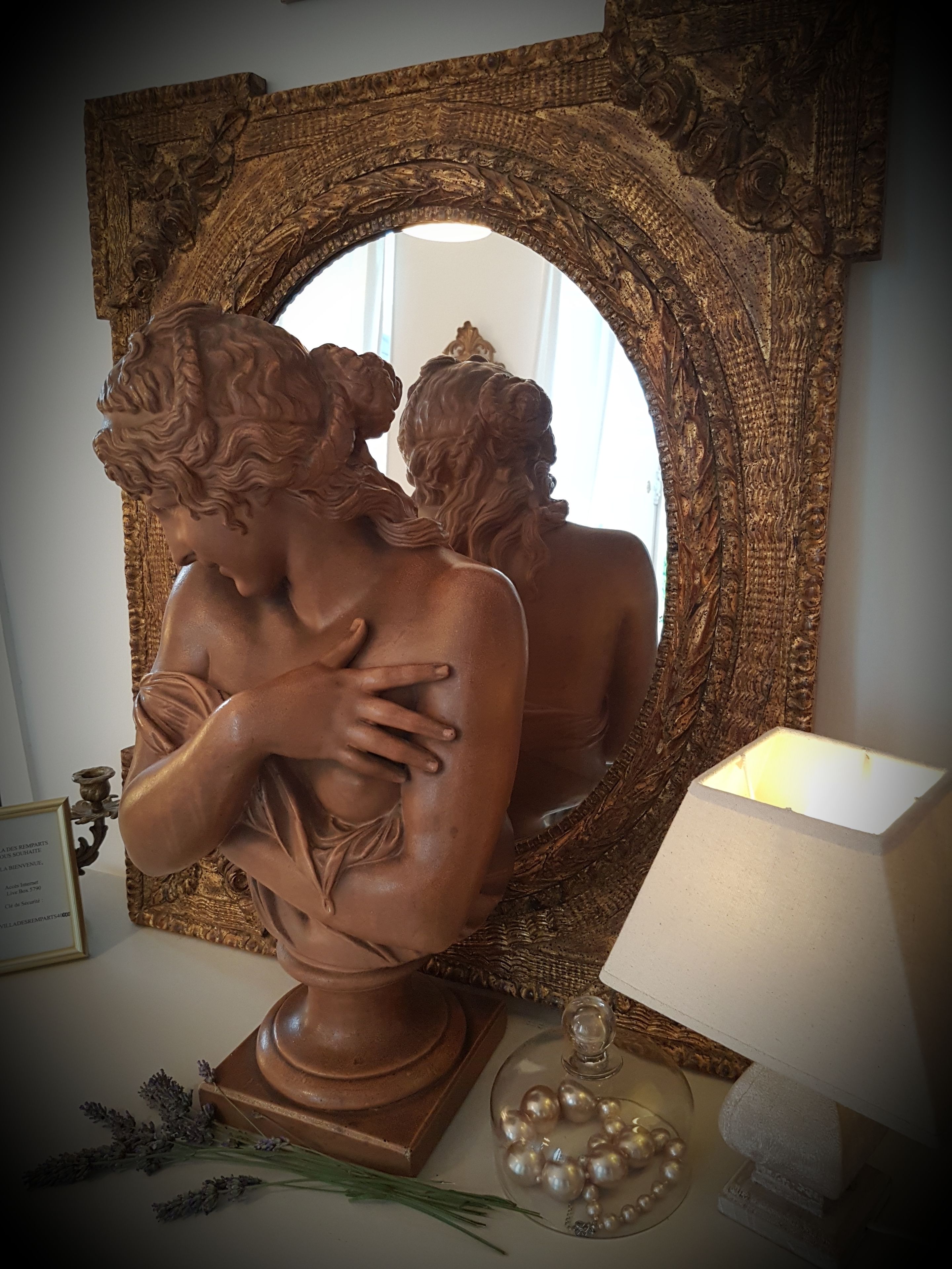Escultura de un hombre y una mujer abrazándose, ubicada sobre un pedestal con un candelabro y objetos decorativos a su lado.
