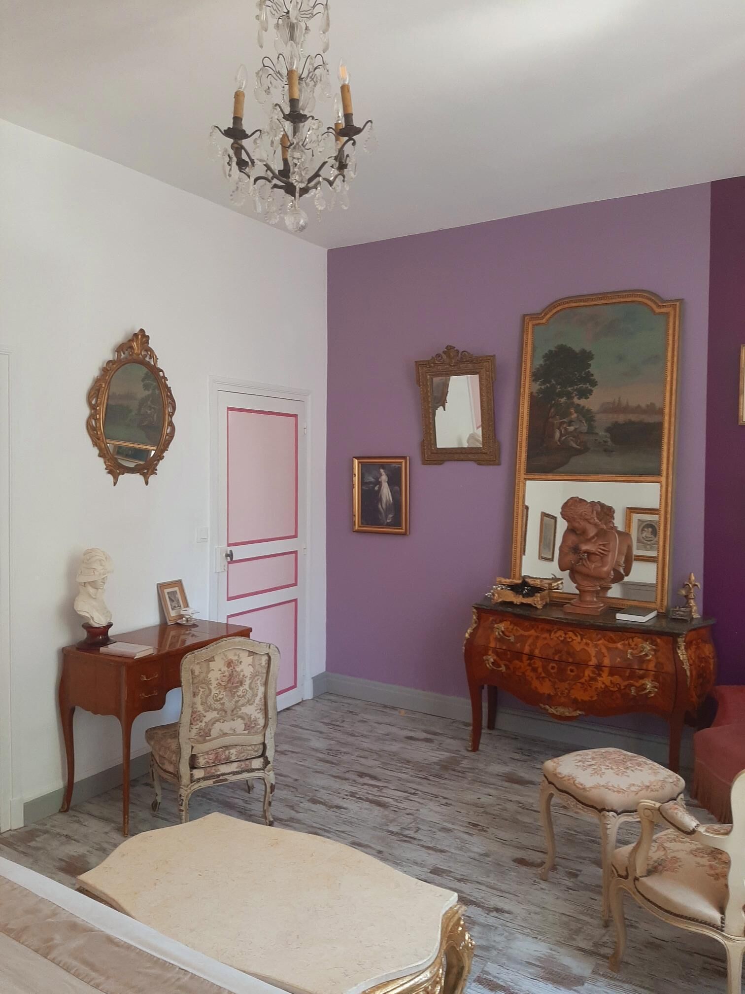 Une pièce comprenant un bureau en bois, une chaise, un canapé, un grand miroir et un lustre.