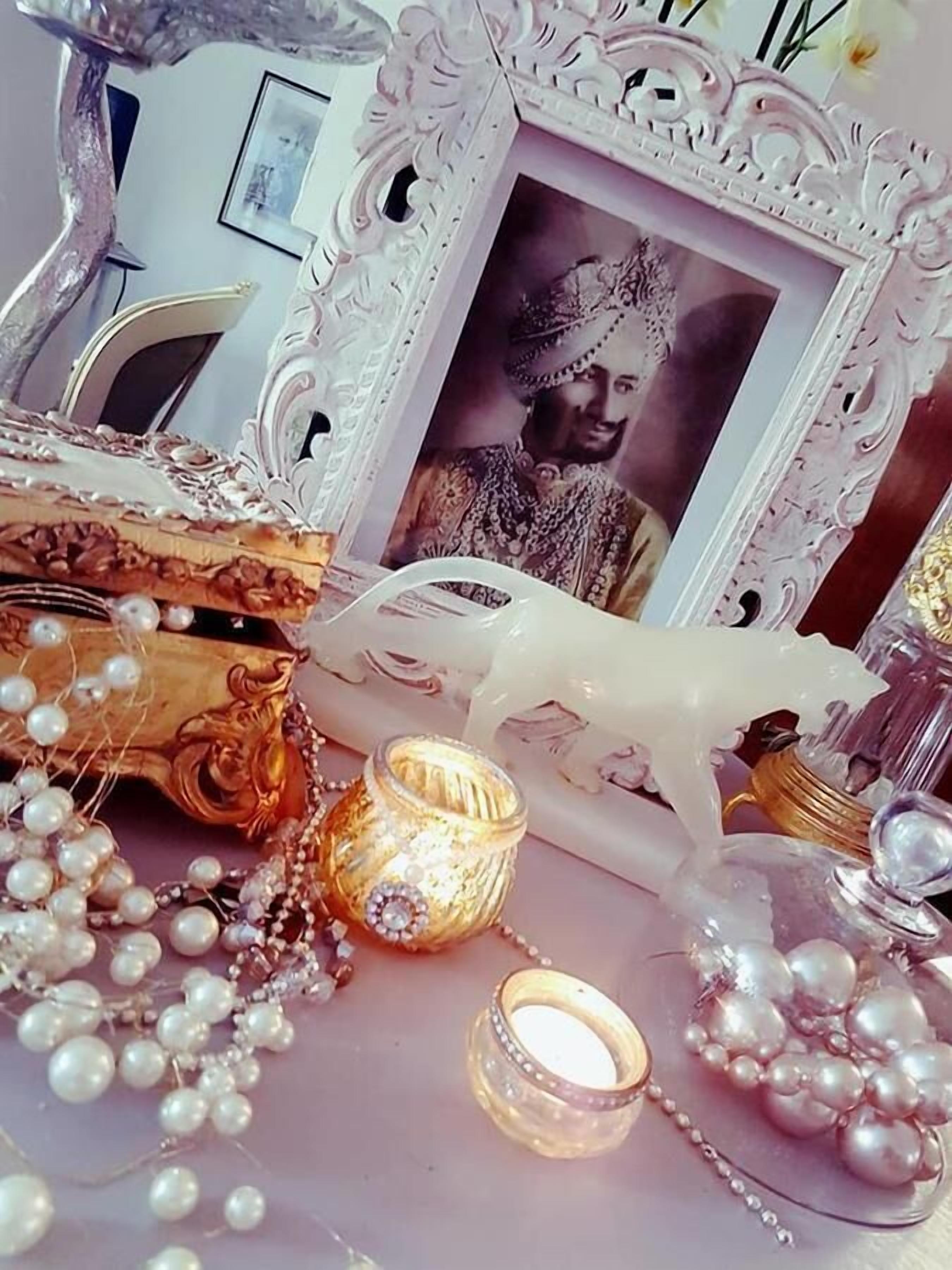 A decorative table with a framed photo, pearls, and a candle.