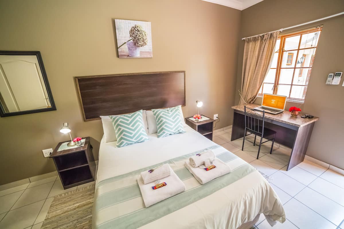 A hotel room with a bed, a desk, a chair, a lamp, and a window with curtains.