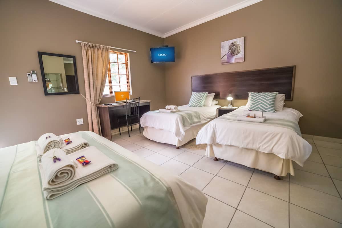 A hotel room with two beds, a desk, a TV, and a window with curtains.