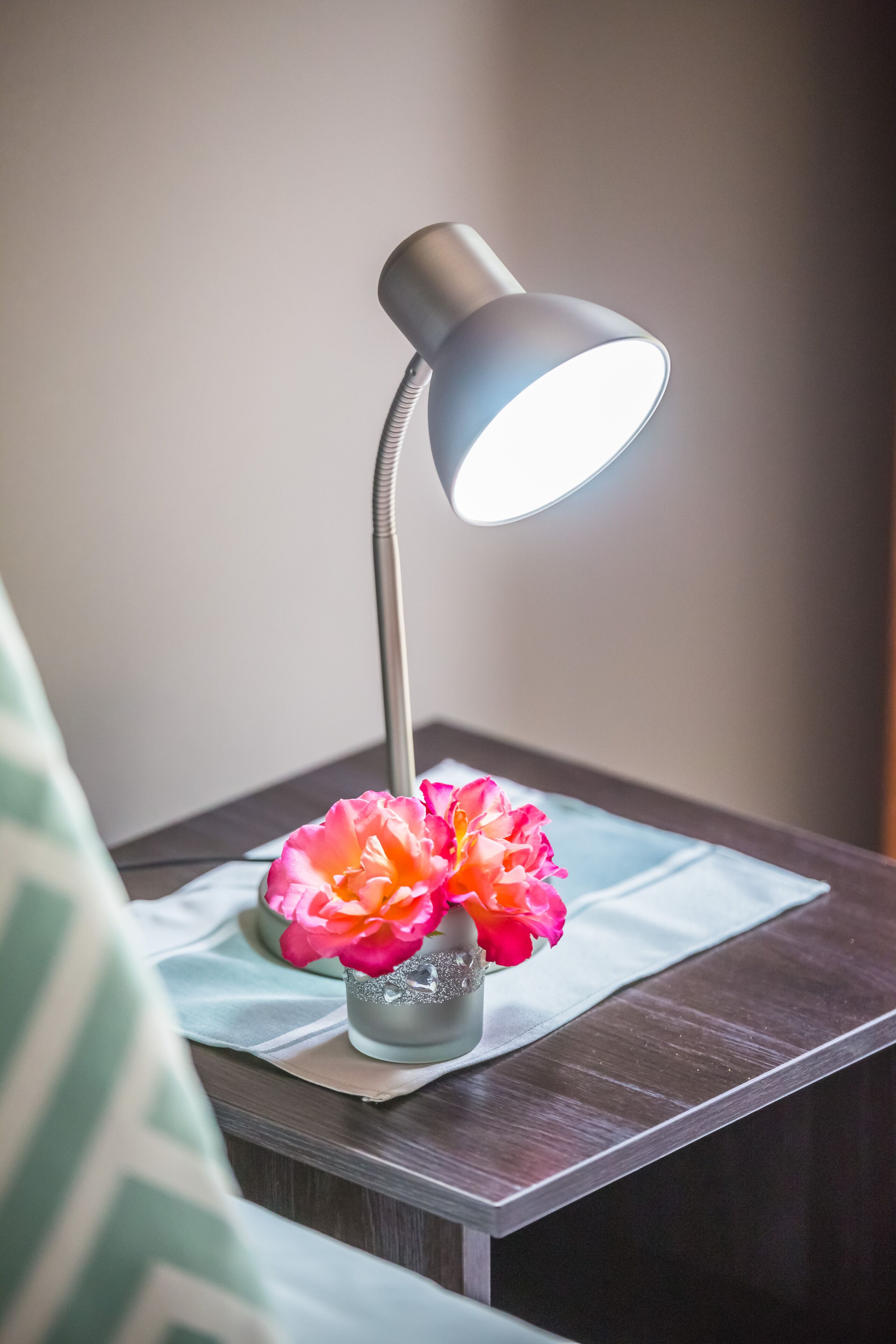 A bedside table with a lamp and a vase of flowers.