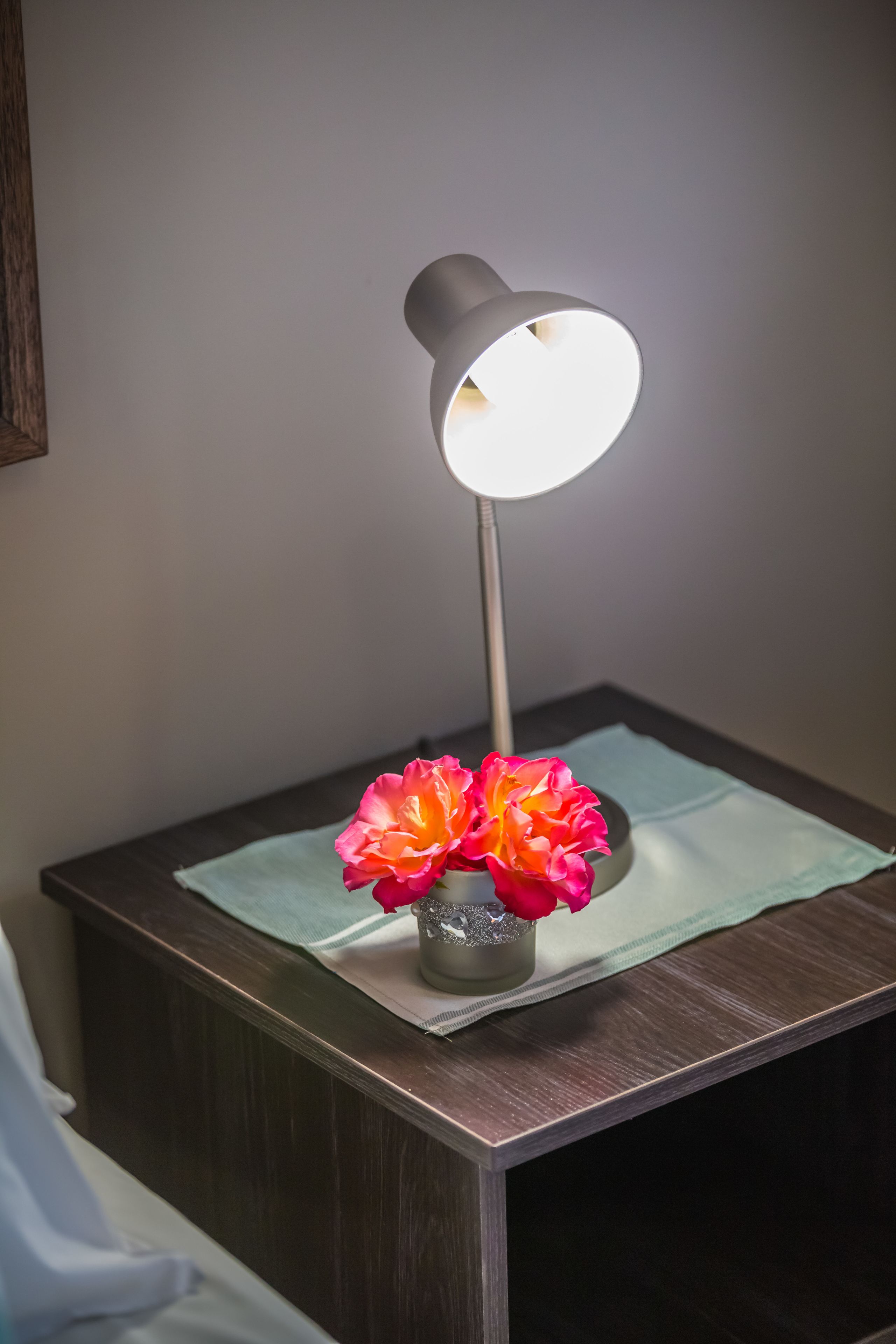 A bedside table with a lamp, a vase with flowers, and a tissue box.