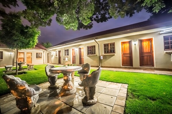A courtyard with a stone table and chairs, a well-manicured lawn, and a building with multiple doors and windows.