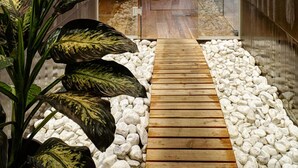 A modern hallway with a wooden walkway, white pebbles, and a large plant. - Hotel Leitner (Rio di Pusteria)