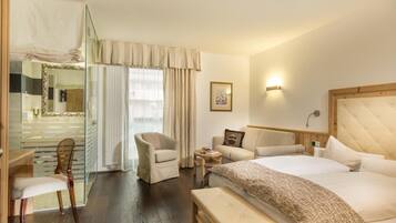 Habitación de hotel con cama, una silla, un banco, una mesita, un sofá, un espejo y una ventana con cortinas.
