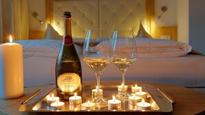 A bed with a tufted headboard, a bottle of Valdobbiadene Prosecco Superiore, two glasses of wine, and multiple lit candles on a tray. - Hotel Leitner (Rio di Pusteria)