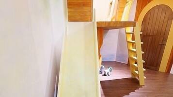 A children's play area with a slide, wooden walls, and a staircase.
