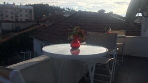 A round table with a red vase and chairs on a balcony overlooking a residential area with houses and trees. - Montenegro central point (Podgorica)
