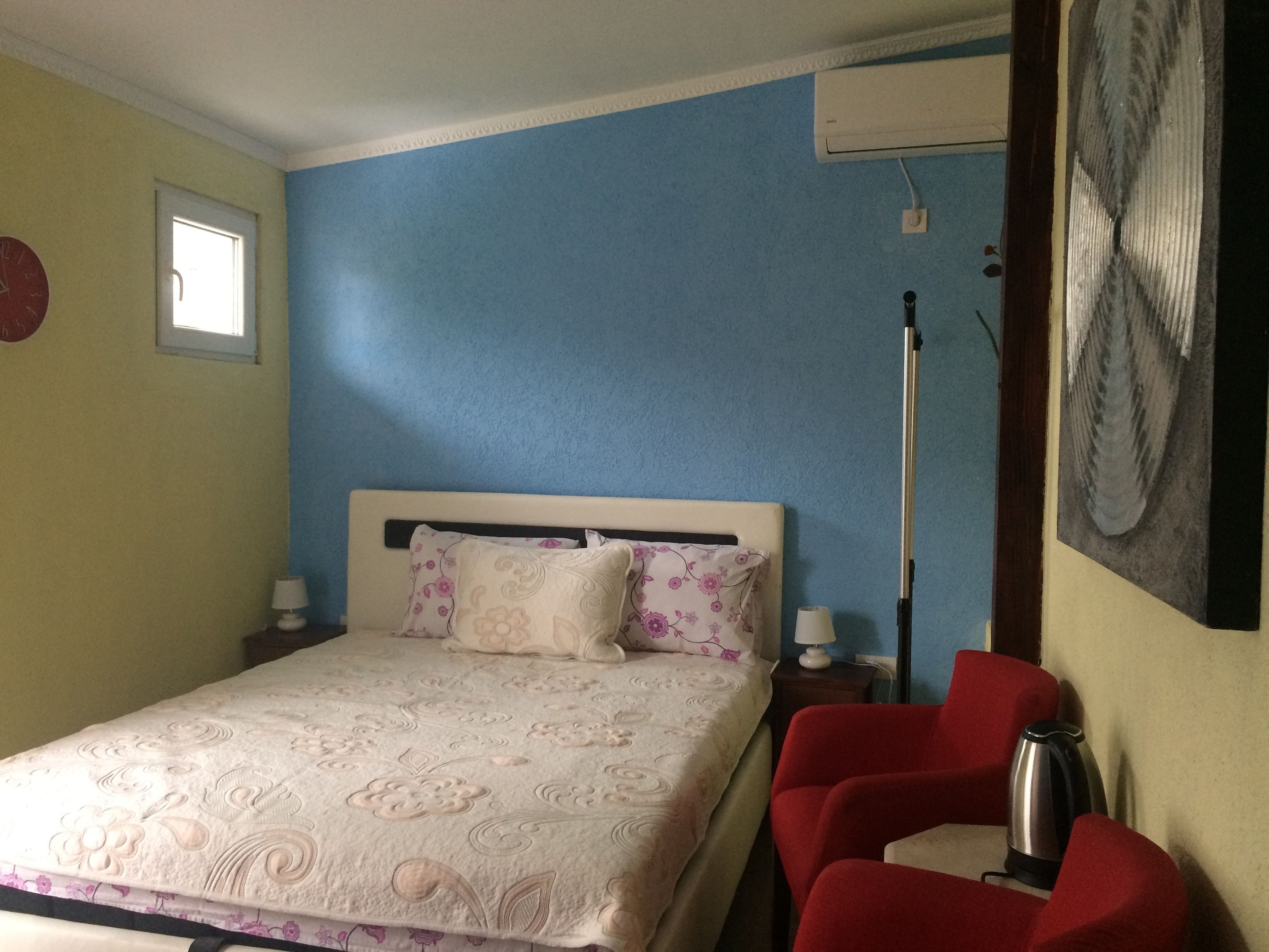 A bedroom with a bed, a red chair, a nightstand, a lamp, and a painting on the wall.