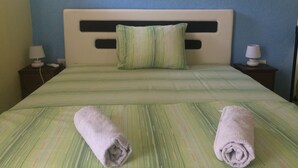 A neatly made bed with green bedding and two rolled towels, a nightstand with a lamp, and a blue wall. - Montenegro central point (Podgorica)