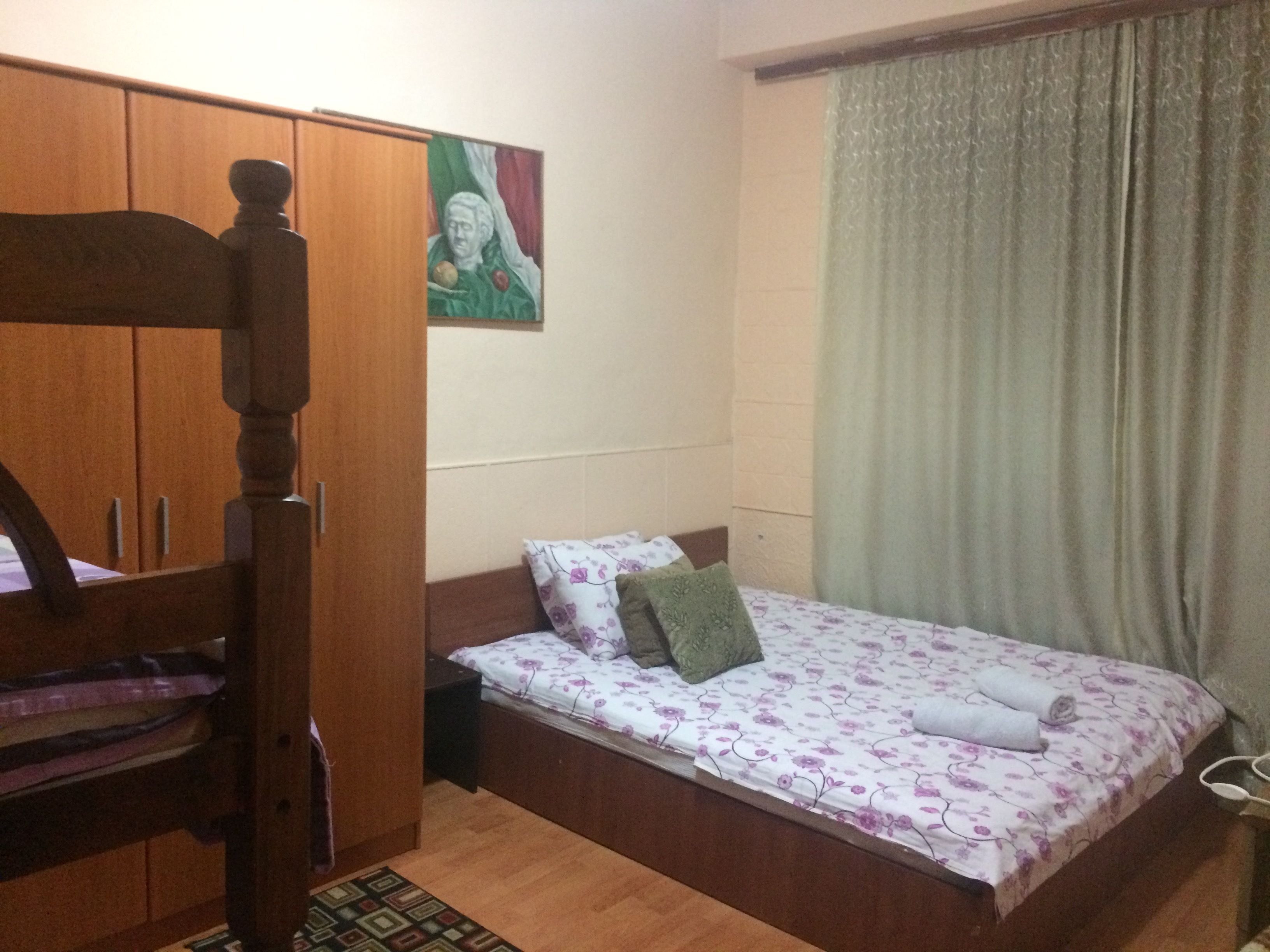 A bedroom with a wooden bed, a small bedside table, a wardrobe, and a painting on the wall.