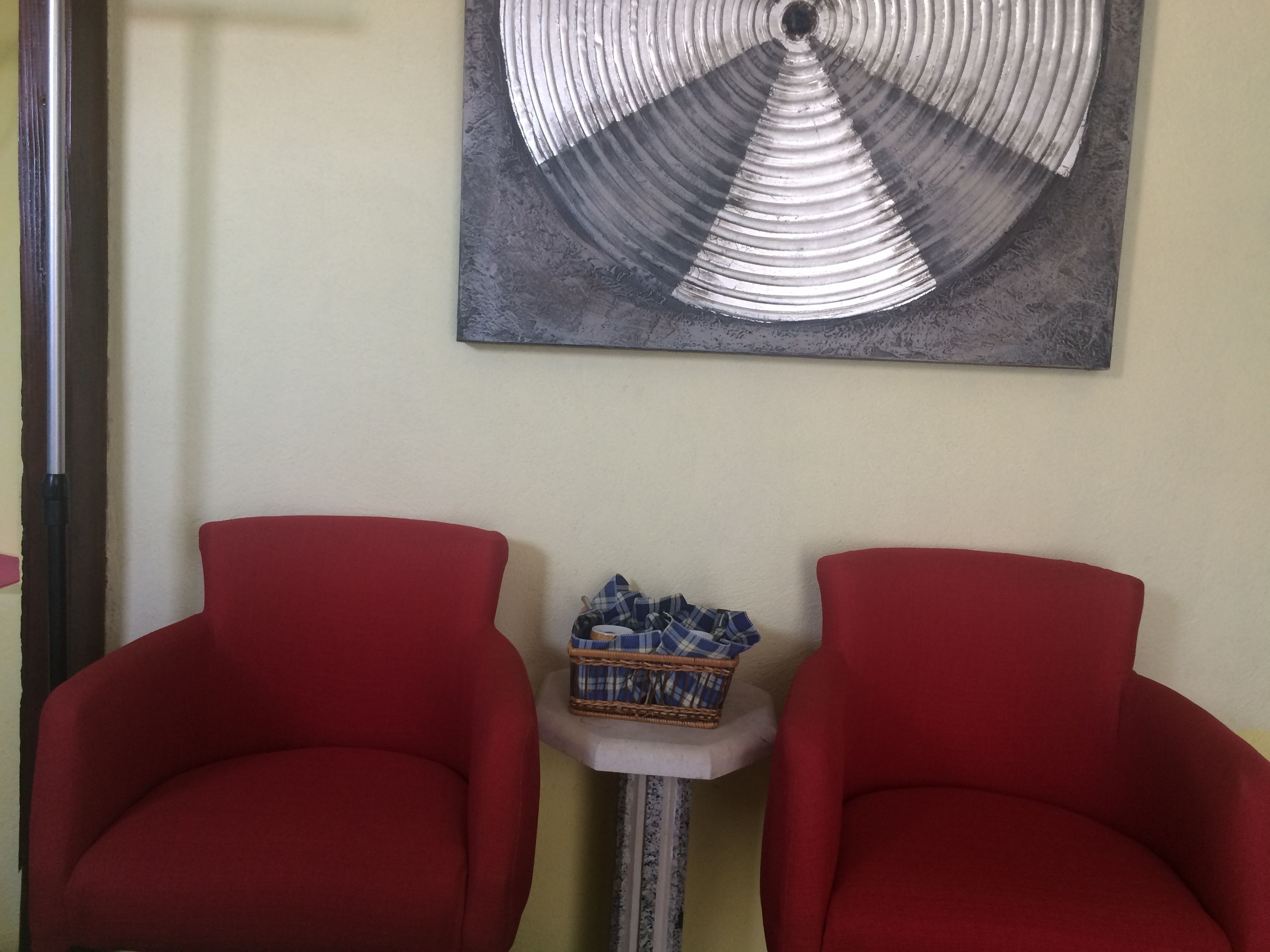 Two red armchairs, a small table with a basket, and a wall-mounted abstract art piece.