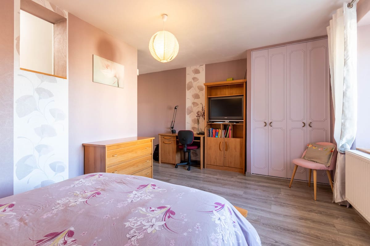 A bedroom with a bed, a desk, a chair, a wardrobe, and a television.