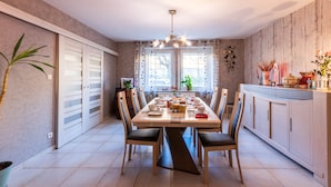 A dining area with a large table, chairs, a chandelier, and a view of the outdoors.