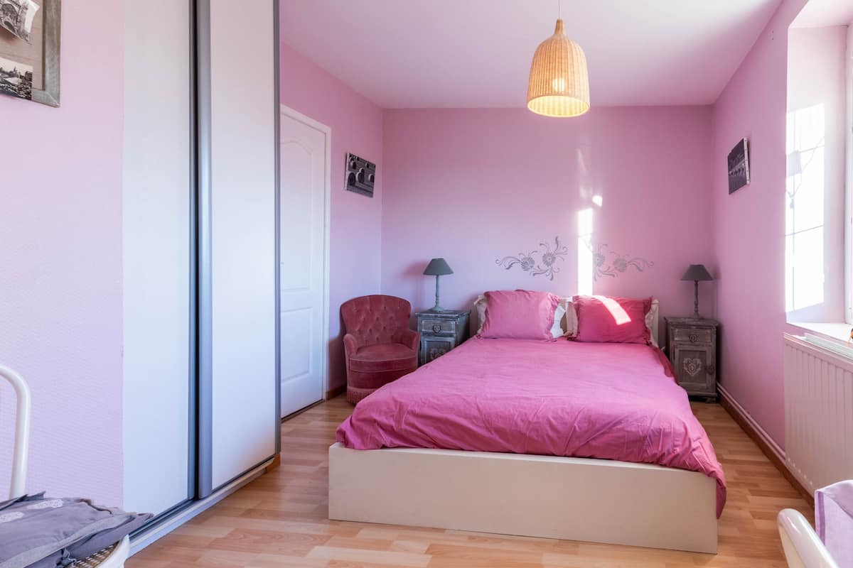 A bedroom with a bed, a chair, a nightstand, and a lamp.