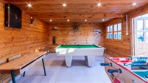 A wooden-paneled room with a pool table, a billiards table, and a bench.