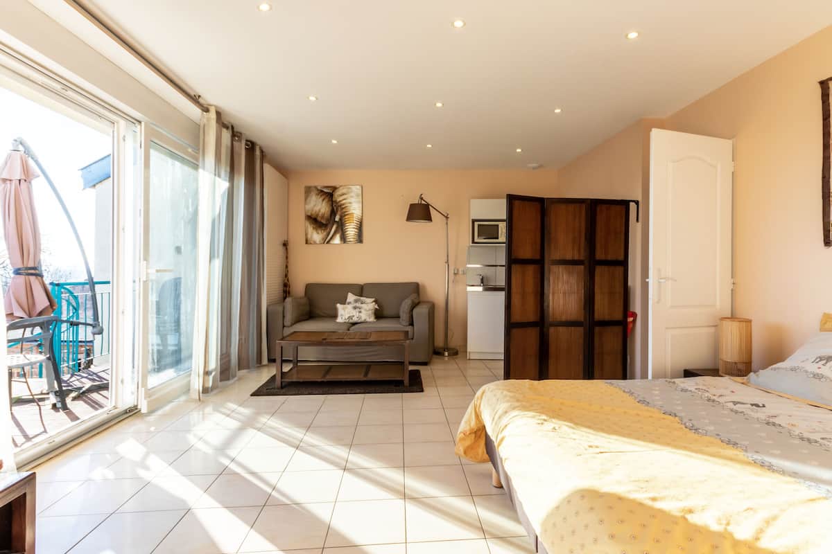 A bedroom with a bed, a sofa, a desk, and a sliding glass door leading to a balcony.