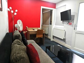 A room with a red wall, a sofa, a desk, a chair, a TV, and a radiator. - Wellesley Hotel (Ilford)