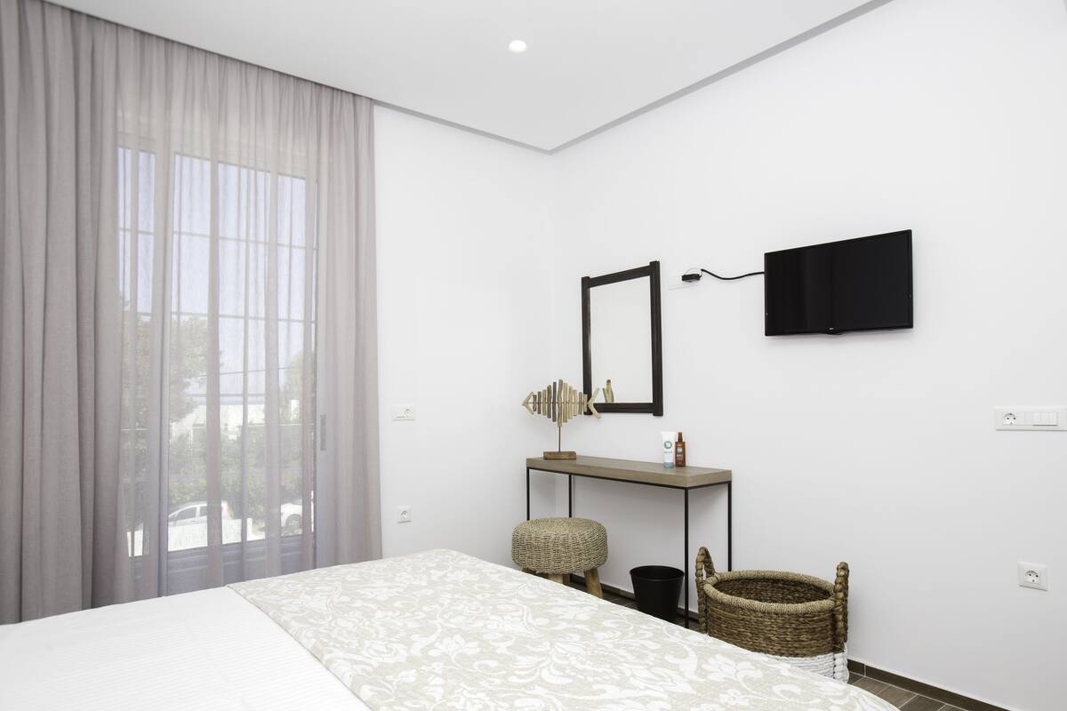 A hotel room with a bed, a desk, a television, and a large window with curtains.