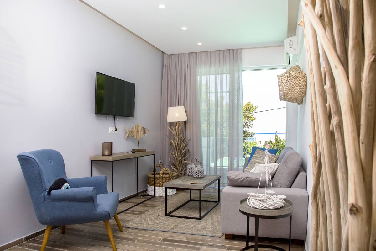 A modern living room with a blue armchair, a grey sofa, a small table, and a TV mounted on the wall.