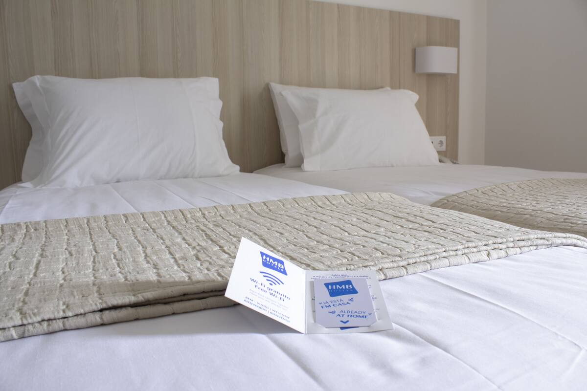 A hotel room with a neatly made bed, a white headboard, and a bedside lamp.