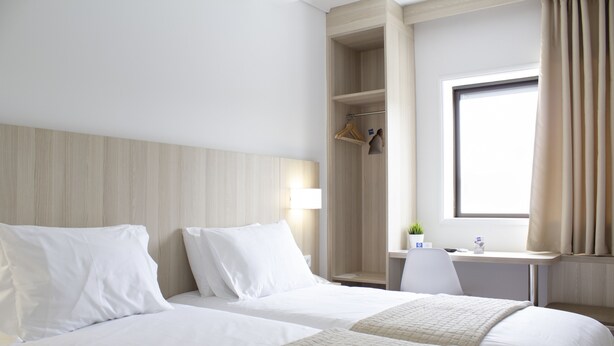 A hotel room with two beds, a desk, a chair, a wardrobe, and a window with curtains. - HMB Fermentelos Hotels (Agueda)