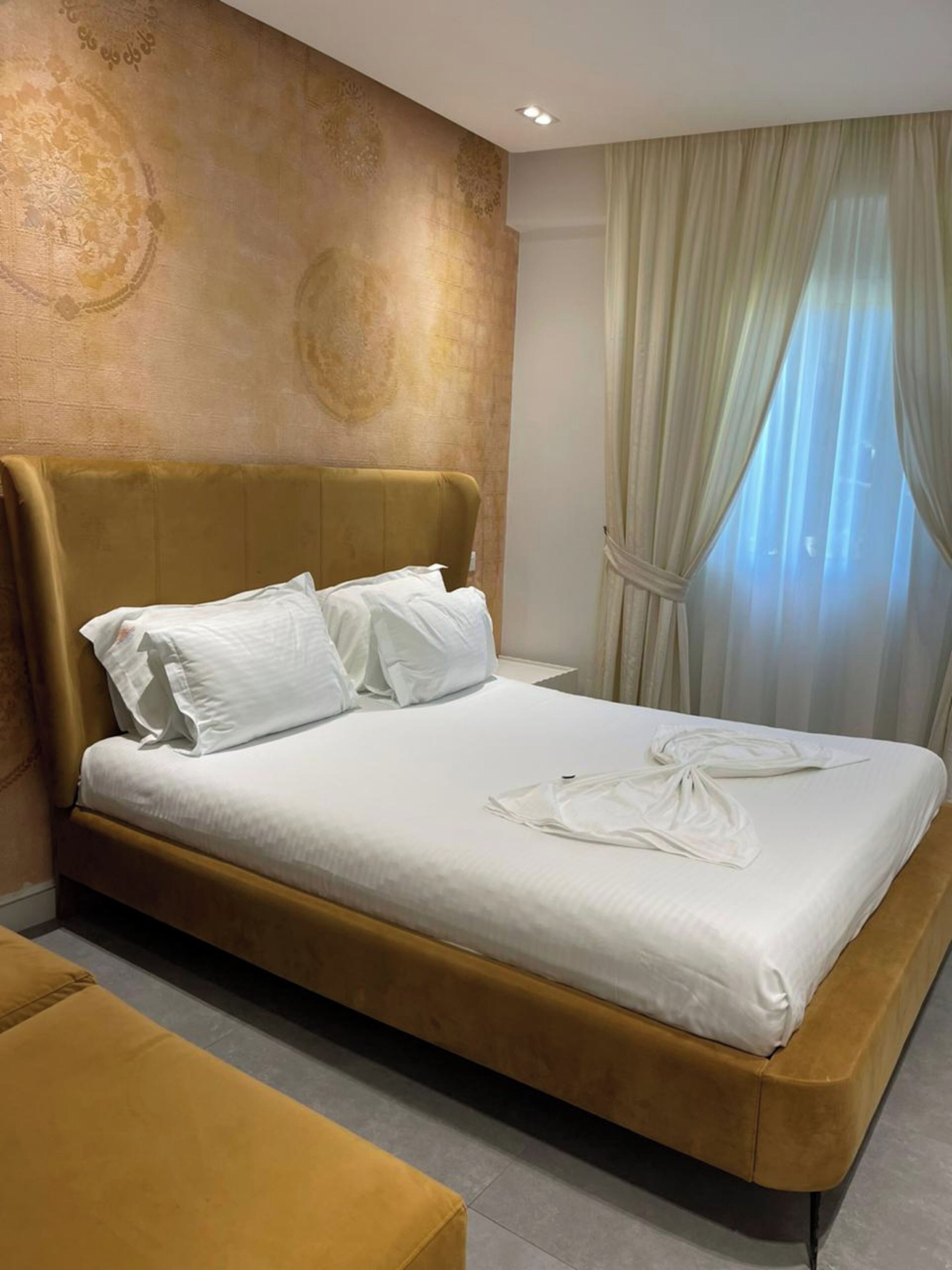 A modern hotel room with a large bed, a headboard, and a window with curtains.