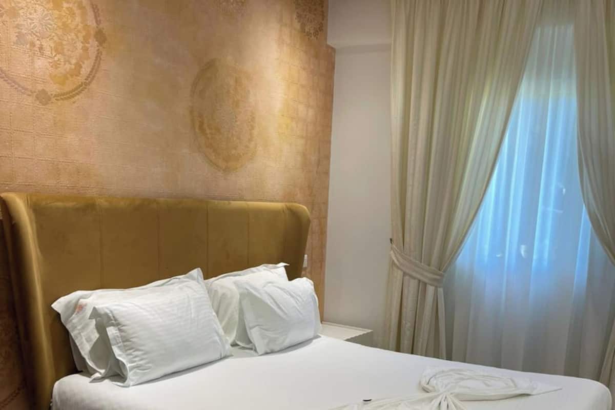 Ein modernes Hotelzimmer mit einem großen Bett, einem Kopfteil und einem Fenster mit Vorhängen.