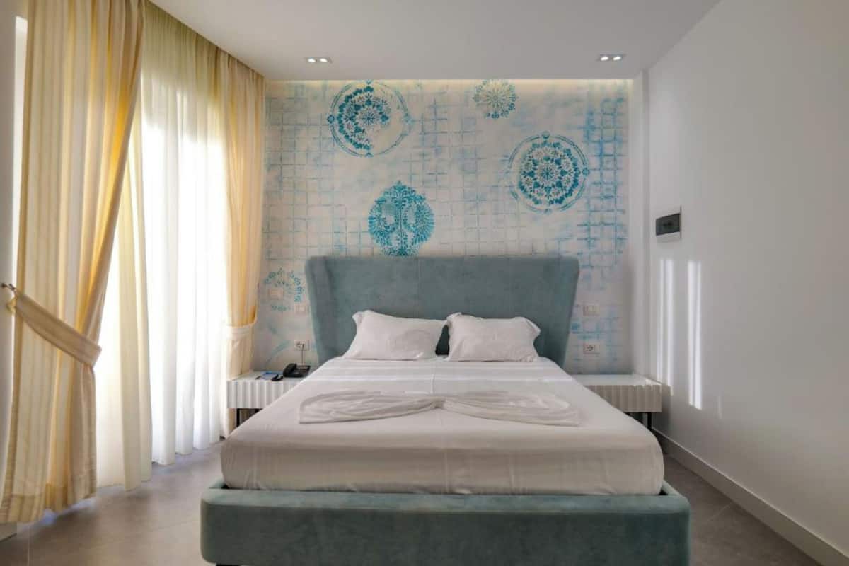 Ein Hotelzimmer mit einem großen Bett, einem Kopfteil, einem Nachttisch und einer Wand mit einem geometrischen Muster.