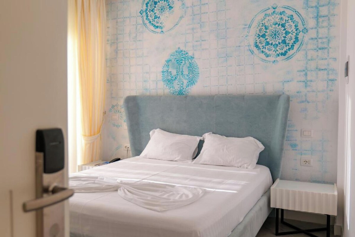 A hotel room with a bed, a bedside table, and a wall with a geometric pattern.