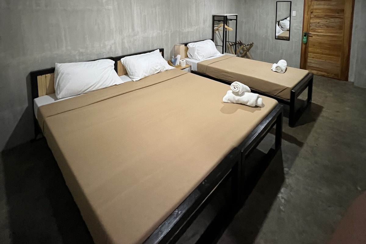 A hotel room with two beds, a wooden door, and an air conditioning unit on the wall.