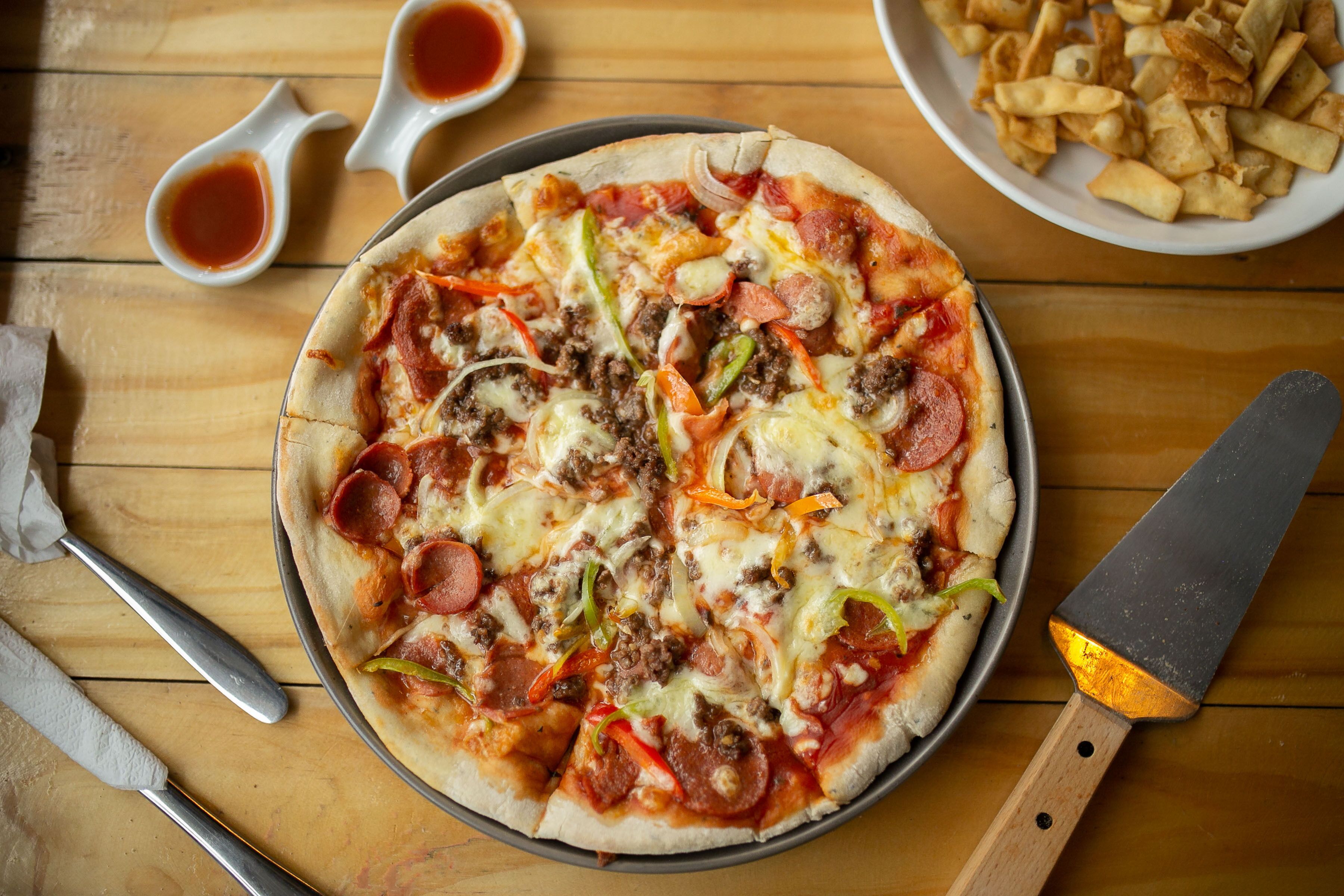 A pizza with pepperoni, sausage, and bell peppers on a wooden table.