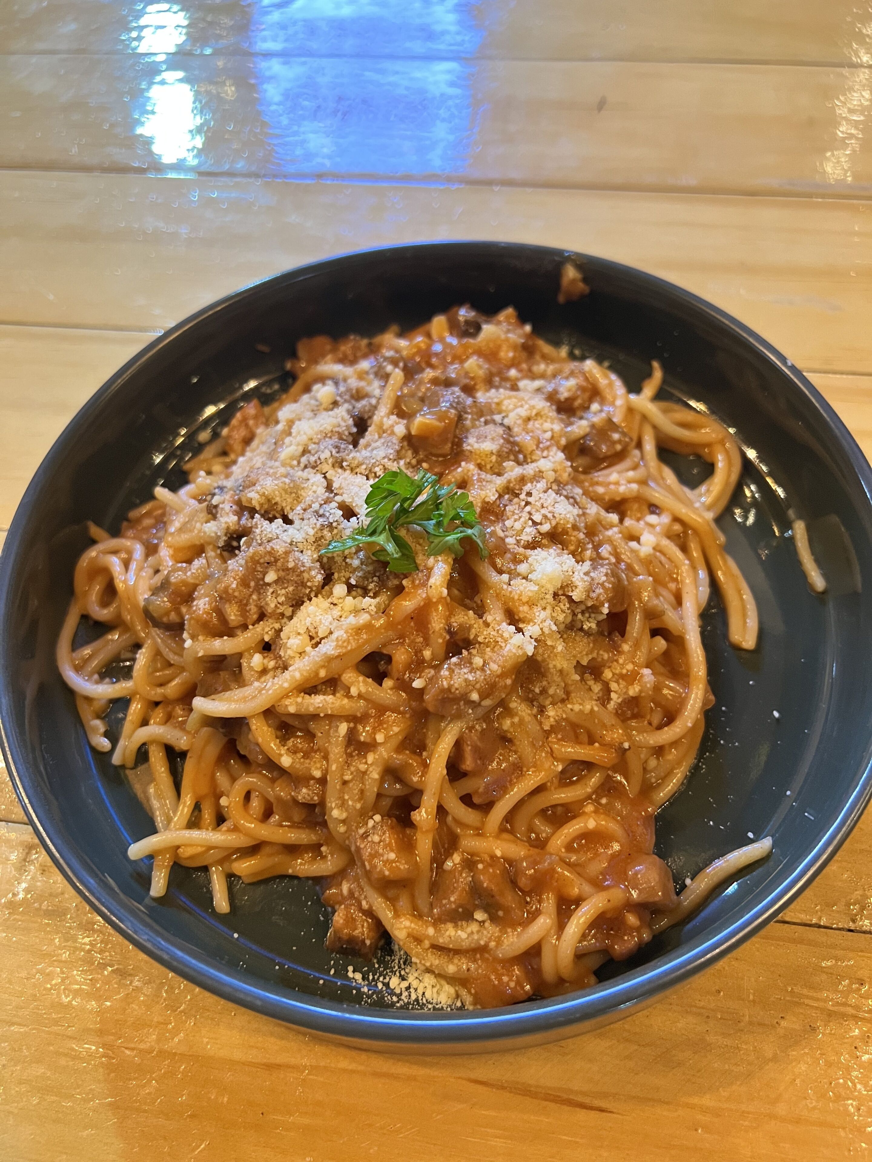 Eine Schüssel Spaghetti mit Tomatensauce, bestreut mit geriebenem Käse und Petersilie, auf einem Holztisch.