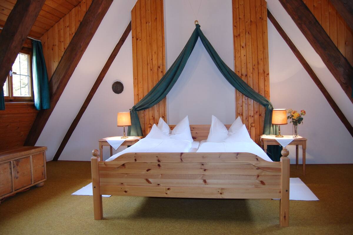 A wooden bed with a canopy in a room with wooden walls and a sloped ceiling.