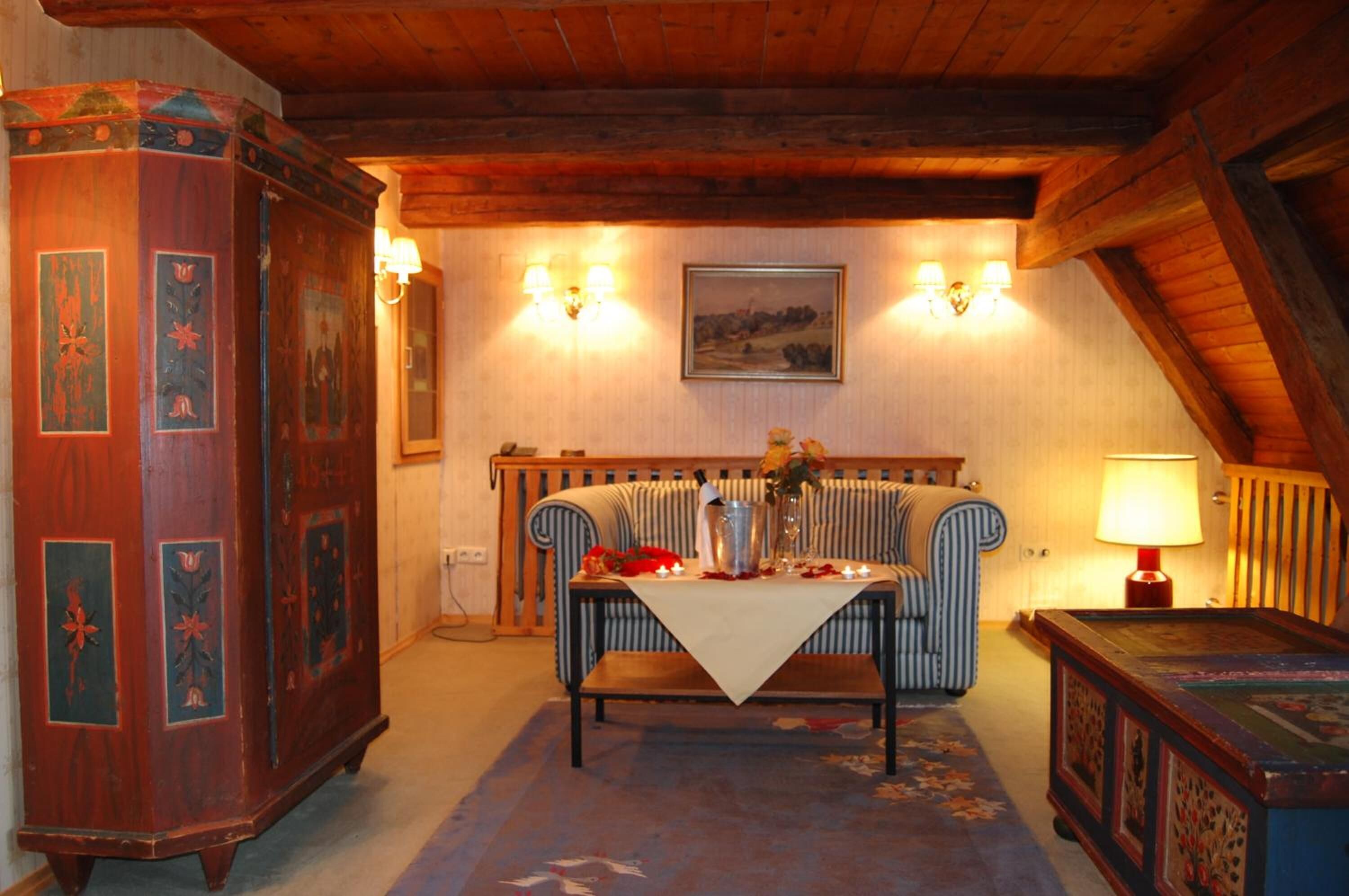 Een gezellige kamer met een houten plafond, een radiator, een eettafel met een wit tafelkleed en een lamp.