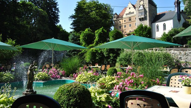 A courtyard with a fountain, outdoor seating, and a historic building in the background. - Schloss Egg (Bernried)