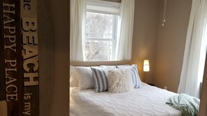 Quarto com cama, ventilador de teto, janela com cortinas e um aviso na parede.