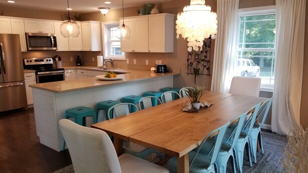Cozinha moderna com armários brancos, uma ilha central e um espaço de jantar com cadeiras azuis.