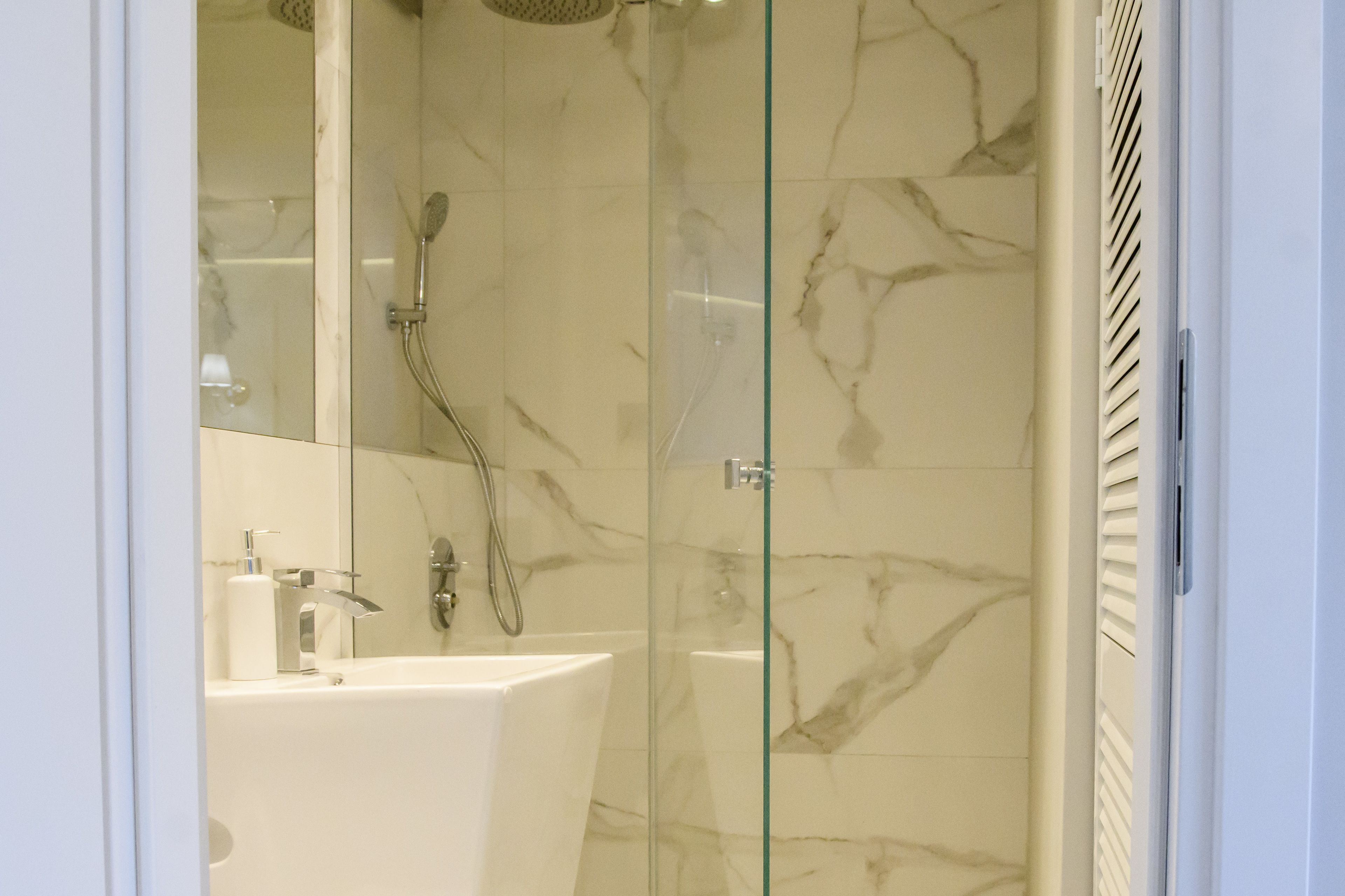 A modern bathroom with a glass-enclosed shower, a white sink, and marble walls.