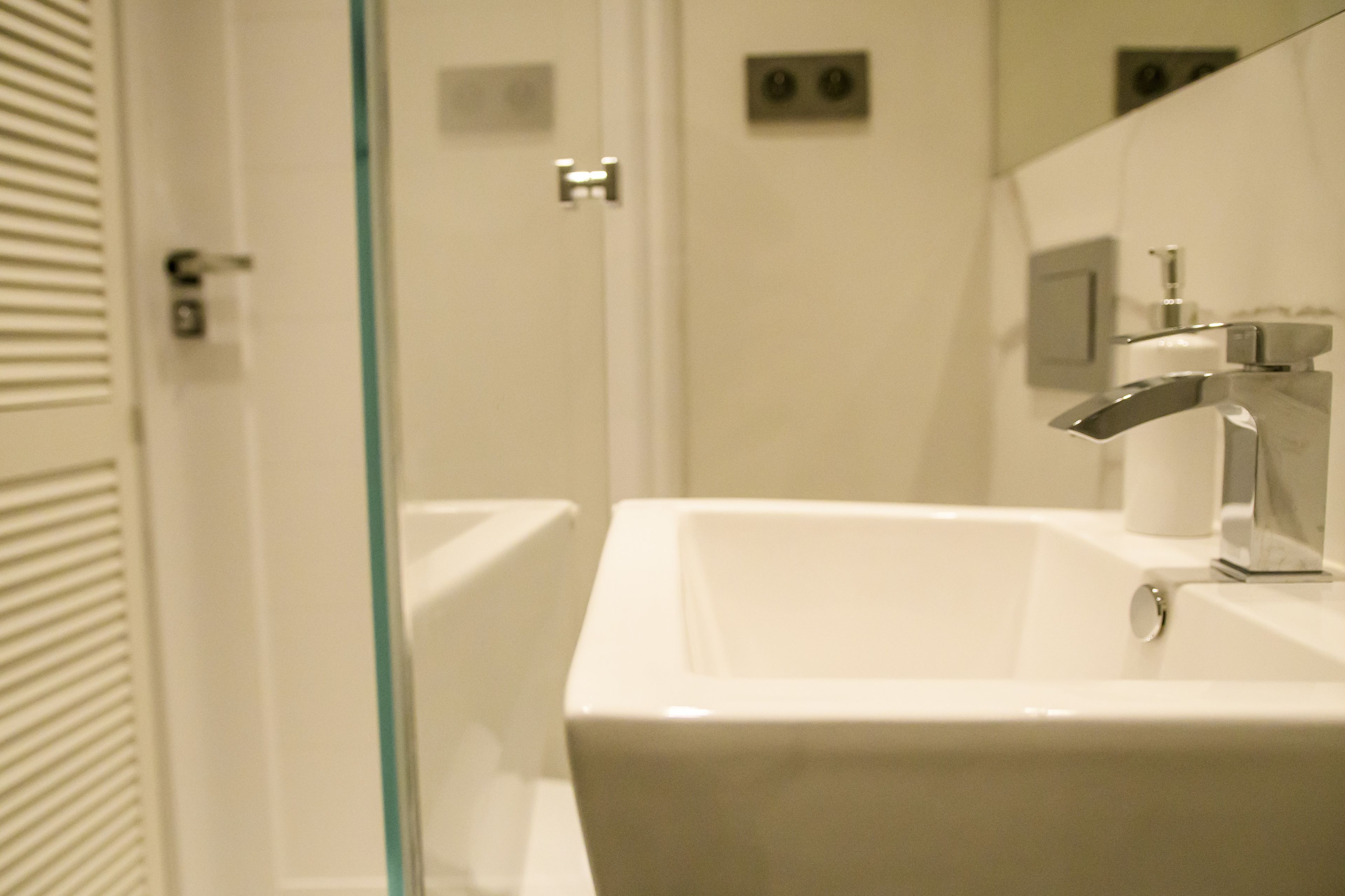 Un baño con un lavamanos blanco, un espejo y un separador de vidrio.
